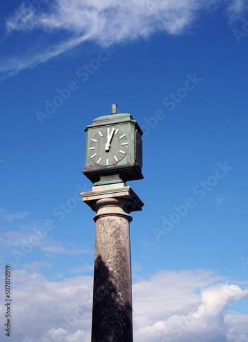 old green metal outdoor clock on a stone pillar in arnside cumbria against a blue cloudy sky