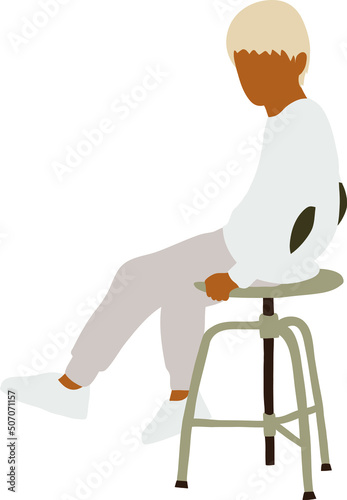 A swarthy boy with blond hair in a white sweater sits on a chair