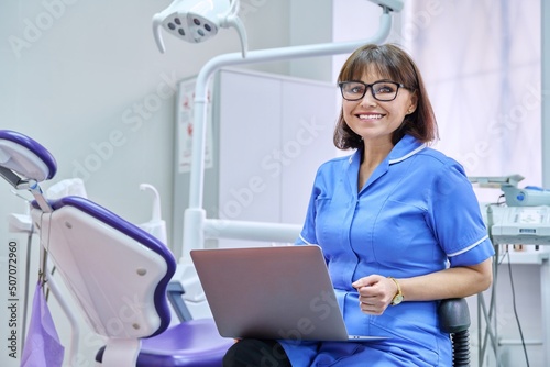 Portrait of dentist nurse sitting in office with laptop in her hands looking at camera photo