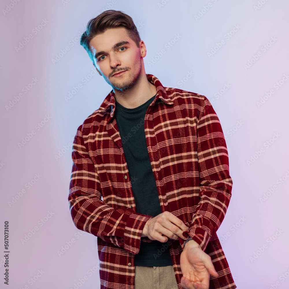 Fashionable handsome guy student with hair in stylish vintage clothes with shirt buttoned sleeve in studio with creative colored light Fashionable handsome guy student with hair in stylish vintage clothes with shirt buttoned sleeve in studio with creative colored light