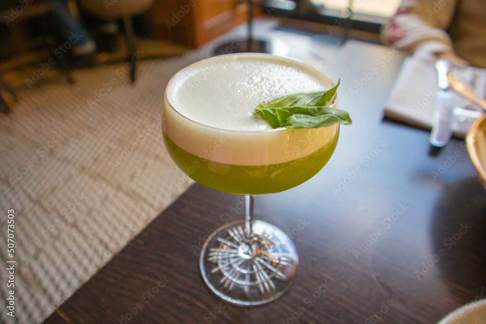 Green alcoholic drink with white foam with green basil leaf in a glass ...