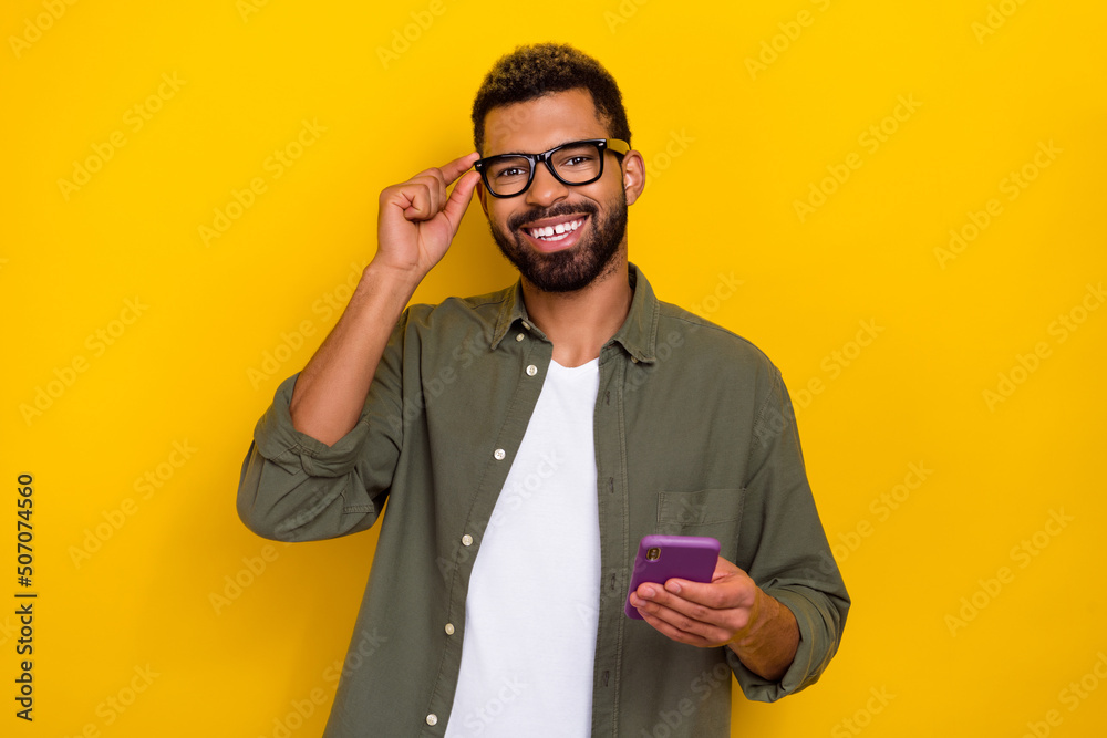 Photo of charming funky guy dressed green shirt arm eyewear chatting modern gadget isolated yellow color background Photo of charming funky guy dressed green shirt arm eyewear chatting modern gadget isolated yellow color background