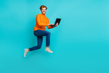 Full length photo of sweet cute man wear orange pullover typing modern device empty space isolated teal color background