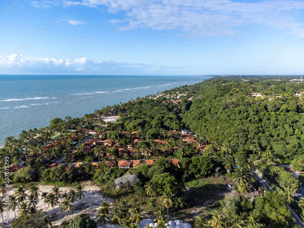 Wonderful paradise beach with the summer sun rising in the middle of the Atlantic Forest. Tourist town Arraial D'Ajuda, Brazil, South America. Aerial drone view.
