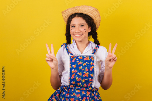 Girl wearing typical clothes for Festa Junina. making peace and love sign with fingers. For the Arraia party photo