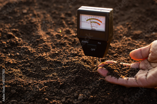 A soil meter and a farmer's hands are picking up soil for planting. photo