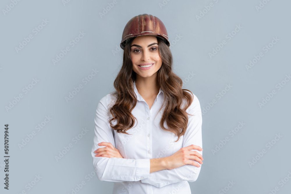Happy young cross-armed female engineer in helmet and hardhat on grey background. Happy young cross-armed female engineer in helmet and hardhat on grey background.