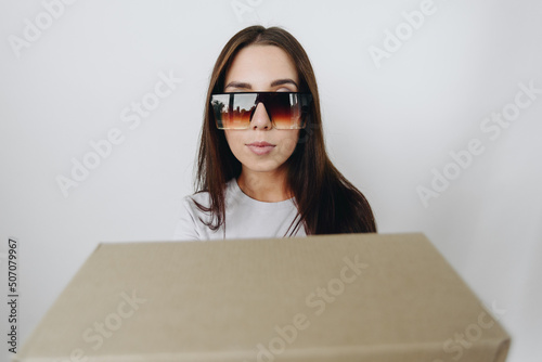 Portrait of a girl in dark glasses in close-up on a white background, a cardboard box in the foreground