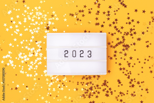 Lightbox with 2023 numbers on a yellow background with golden stars confetti.
