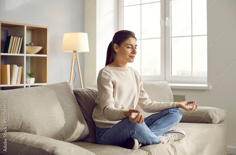 Calm young Caucasian woman sit on couch with mudra hands practice yoga meditate. Relaxed girl have meditation session on sofa at home, relieve negative emotions breathe. Stress free concept. Calm young Caucasian woman sit on couch with mudra hands practice yoga meditate. Relaxed girl have meditation session on sofa at home, relieve negative emotions breathe. Stress free concept.