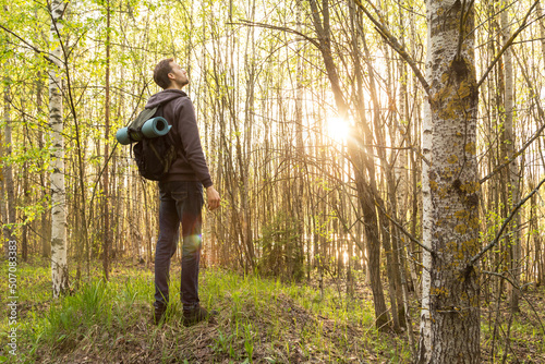 Man, tourist hiking, walking in spring summer green forest with backpack in sunlight at nature