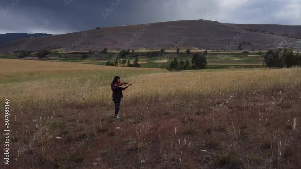 Mujer joven tocando violin en una montaña al atardecer. Concepto de musica y tradiciones.