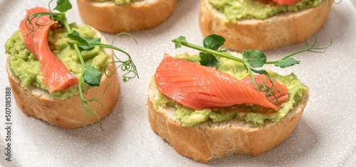 Sandwich with smoked or salted salmon, avocado guacamole and microgreens. Side view, selective focus. Banner.