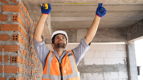 Worker Middle Eastern, Turkish, Iranian handsome engineer is working happily using a tape measure. Male workers wear personal protective equipment such as hard hats, gloves and reflective vests. photo