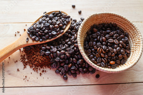 Coffee beans in wooden spoon and ground coffee in wicker tray isolated on wooden background closeup. 