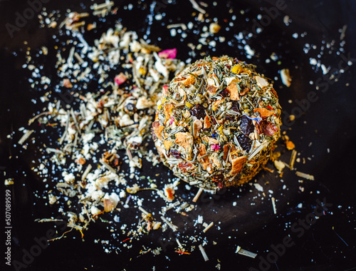 The round head of the French spicy cheese Boulette d'Avesnes sprinkled with different herbs, lies on a black plate. Close-up. Brin d'Amour photo