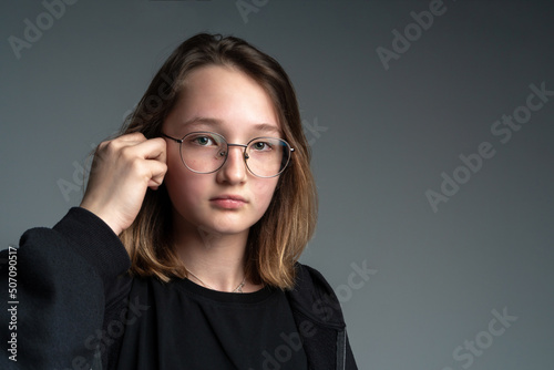 Pensive teenage girl in glasses portrait on a gray background. Space for text