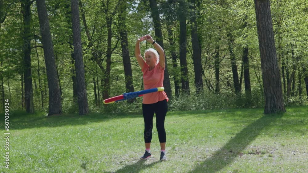 senior elderly woman female doing hula hoop exercises sport in park sunny day. concept healthy lifestyle, loose weight, flat belly. active retirement, outdoor activities for mature people. senior elderly woman female doing hula hoop exercises sport in park sunny day. concept healthy lifestyle, loose weight, flat belly. active retirement, outdoor activities for mature people.