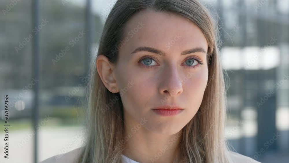 Portrait of confident young woman with blond hair looking at camera outdoor. Serious female standing near glass wall of office building. Concept of people, lifestyles and emotions. Portrait of confident young woman with blond hair looking at camera outdoor. Serious female standing near glass wall of office building. Concept of people, lifestyles and emotions.