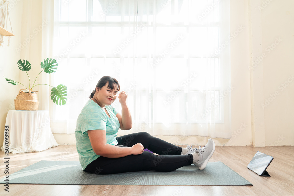 Asian female plus size in sportwear training on yoga mat. Training in loss weight course online video in tablet. Healthy lifestyle concept. Asian female plus size in sportwear training on yoga mat. Training in loss weight course online video in tablet. Healthy lifestyle concept.