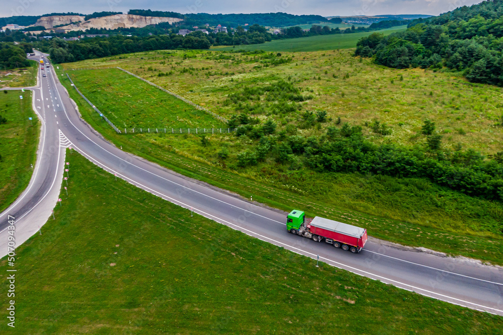 trucks driving on asphalt road along the green fields. seen from the air. Aerial view landscape. drone photography. cargo delivery