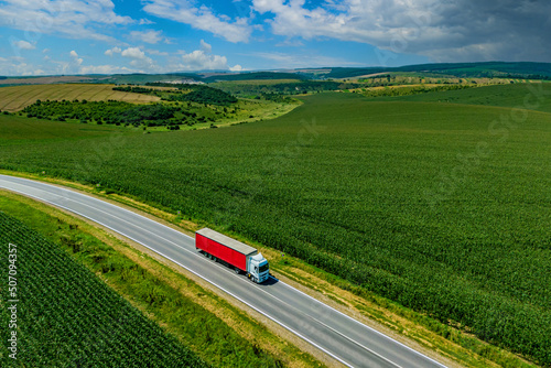 red truck driving on asphalt road along the green fields. seen from the air. Aerial view landscape. drone photography. cargo delivery . cargo delivery and transportation concept