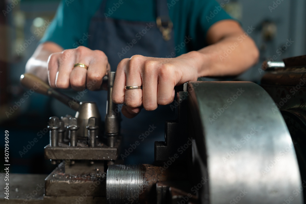 Close-up of a steel lathe with an iron insert, and iron is being machined in the machine, with mechanics closely operating the machine, in a small family-owned factory.. Close-up of a steel lathe with an iron insert, and iron is being machined in the machine, with mechanics closely operating the machine, in a small family-owned factory..