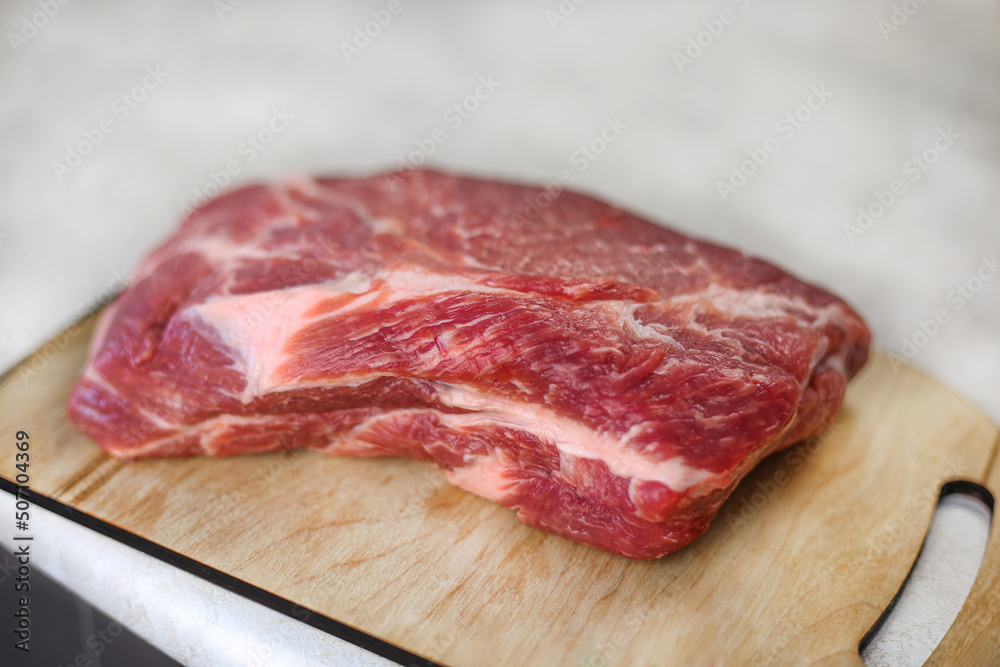 Big fresh piece of meat on wooden cutting board on light kitchen table