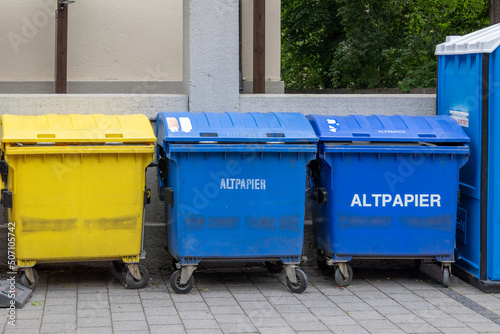 Two blue waste paper garbage cans and a yellow garbage can for plastic waste on the street in a German city center, waste separation in Germany. 
