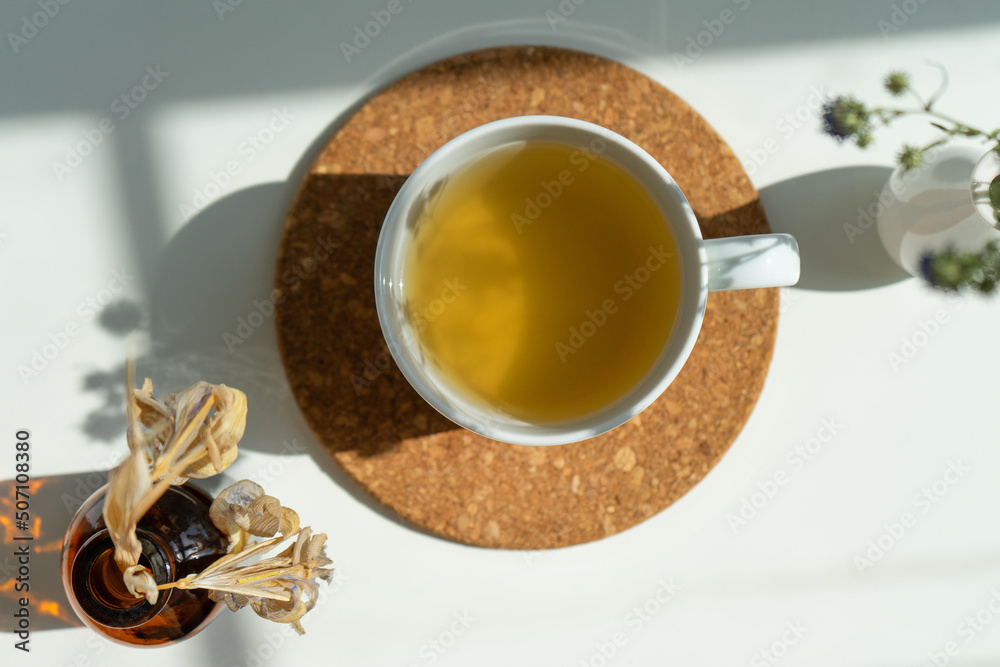 Fototapeta premium tea on a stand in a white mug with a vase of flowers on a white background in sunlight.