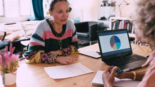 Two business women sitting at table in office discuss topics.