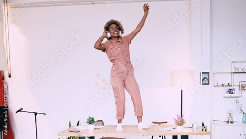 Beautiful office worker in casual clothes is dancing on desk in office wearing headphones enjoying break from work