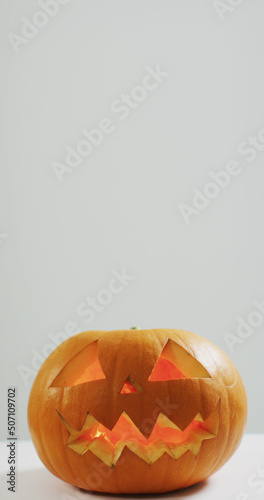 Vertical image of close of lit carved halloween pumpkin on white background