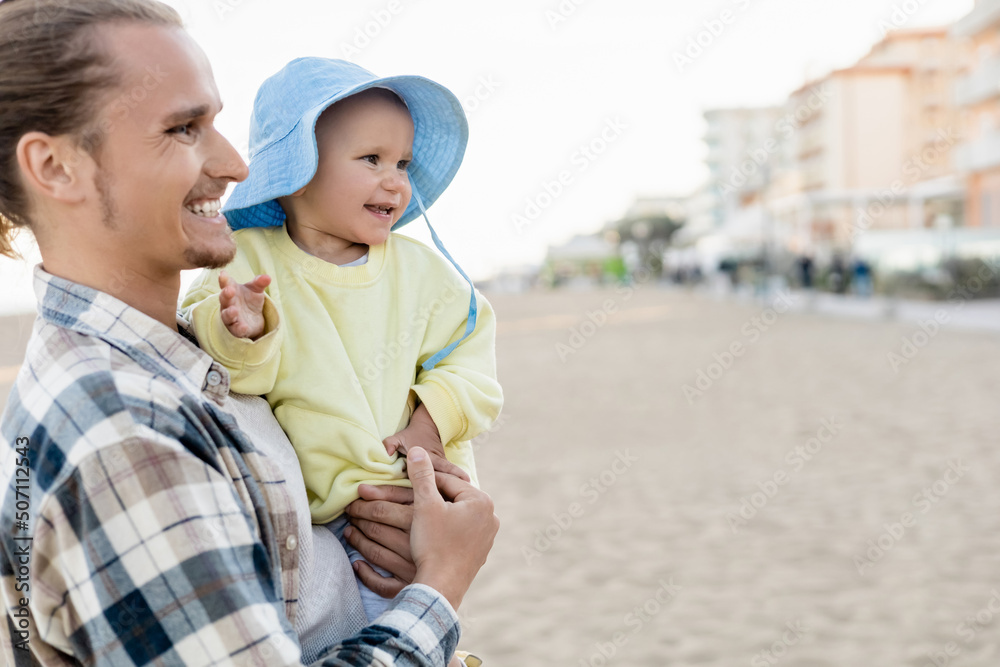 Smiling father and baby girl looking away on beach in Italy. Smiling father and baby girl looking away on beach in Italy.