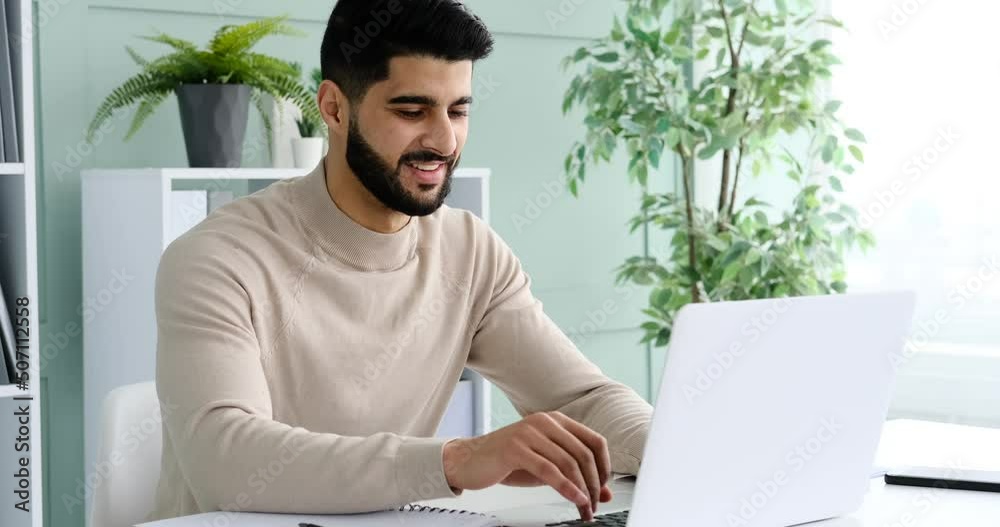 Happy young businessman typing on laptop at office