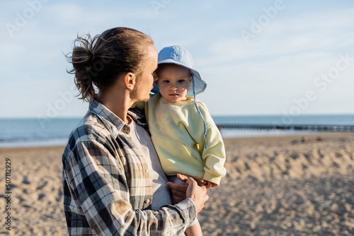 Long haired father looking at baby girl in panama hat on beach in Italy. © LIGHTFIELD STUDIOS