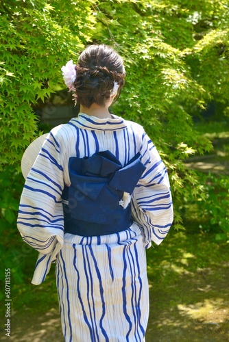 緑の新緑を背景に浴衣を着た若く美しい女性の後ろ姿