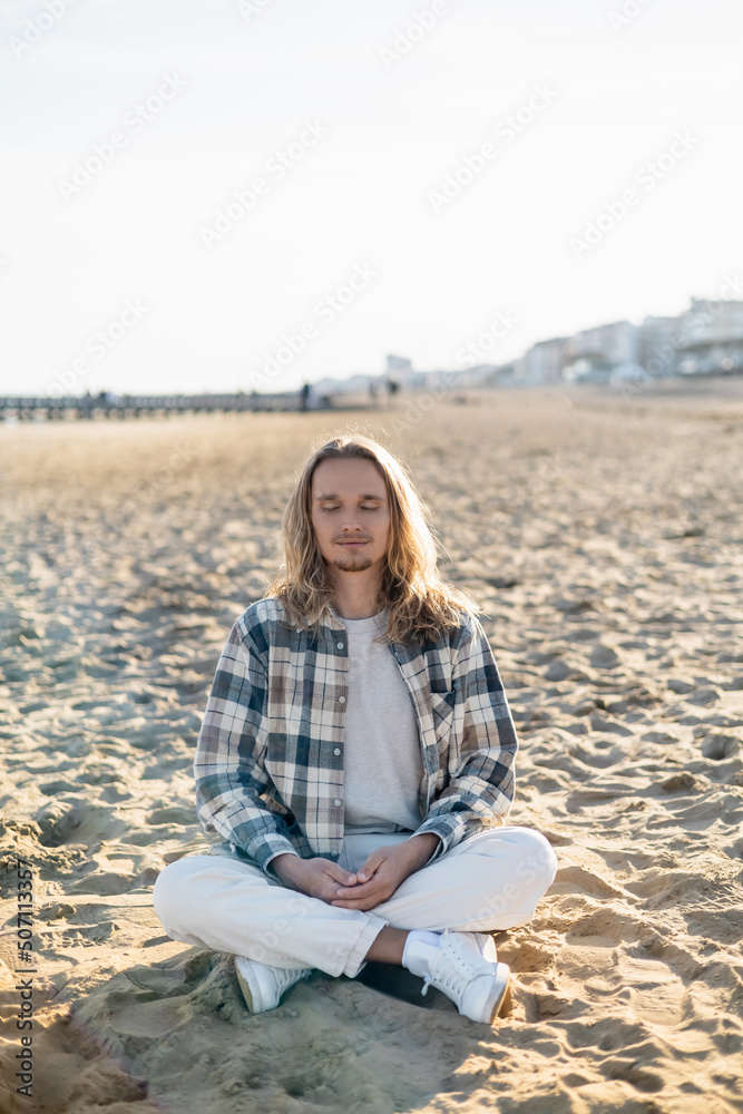 Young man with closed eyes meditating on beach in Italy.