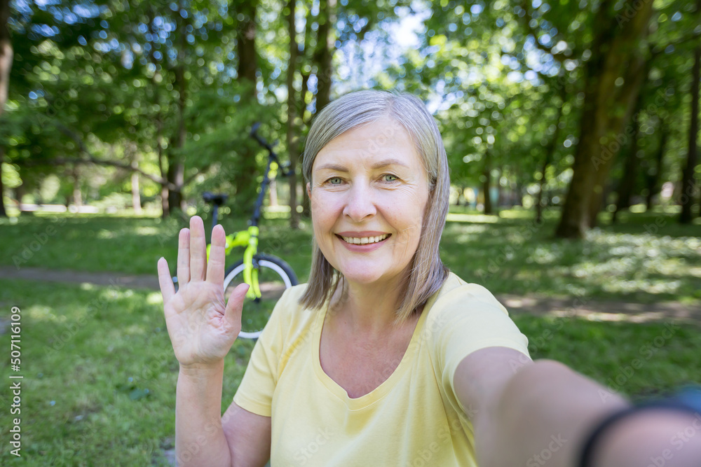 Senior active woman in the park talking on a video call, looking at the smartphone camera, smiling on a morning walk in the park