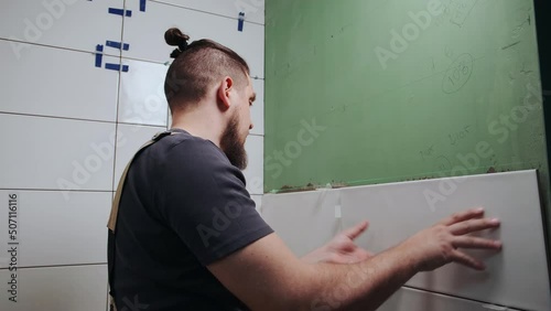 Tiler laying ceramic tiles on the wall in the bathroom
