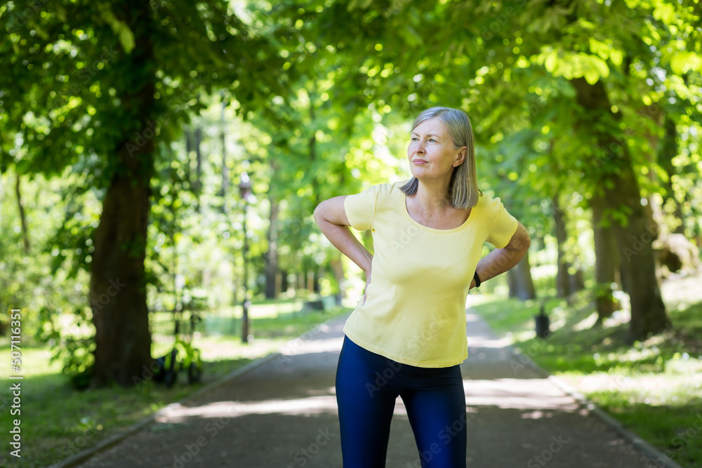 Senior active woman on a walk in the park injured her back, pensioner on a jog on a summer day