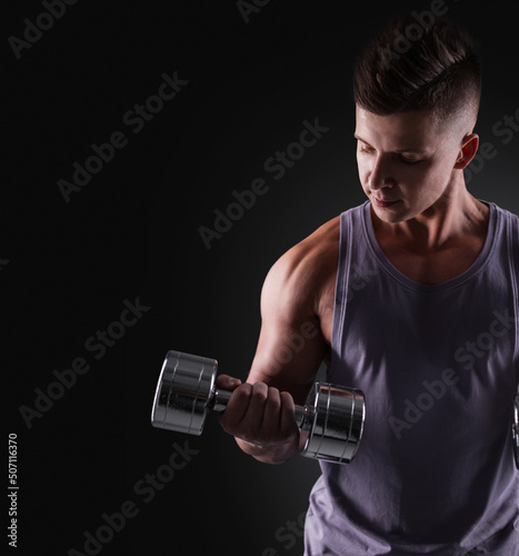 Muscular athletic handsome man with a metal dumbbell trains biceps isolated on black background. Sporty guy. Copy space for design and text
