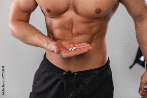 Muscular athletic guy with a naked torso is holding vitamins and steroids pills. Sports and supplements. Healthy lifestyle and medicine