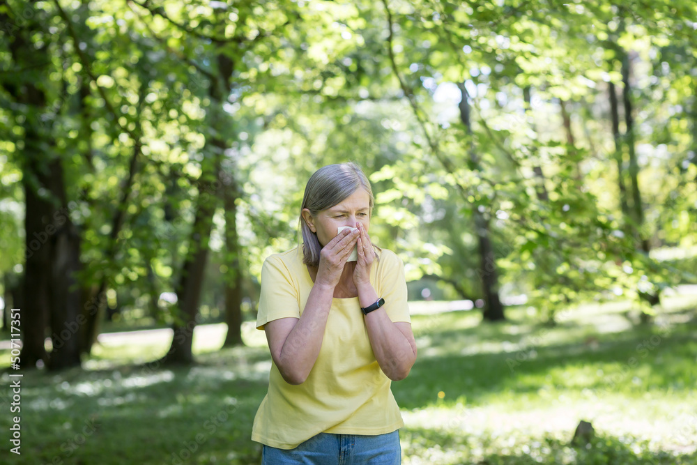 An elderly woman in the park with allergies has a runny nose and sneezes near trees An elderly woman in the park with allergies has a runny nose and sneezes near trees
