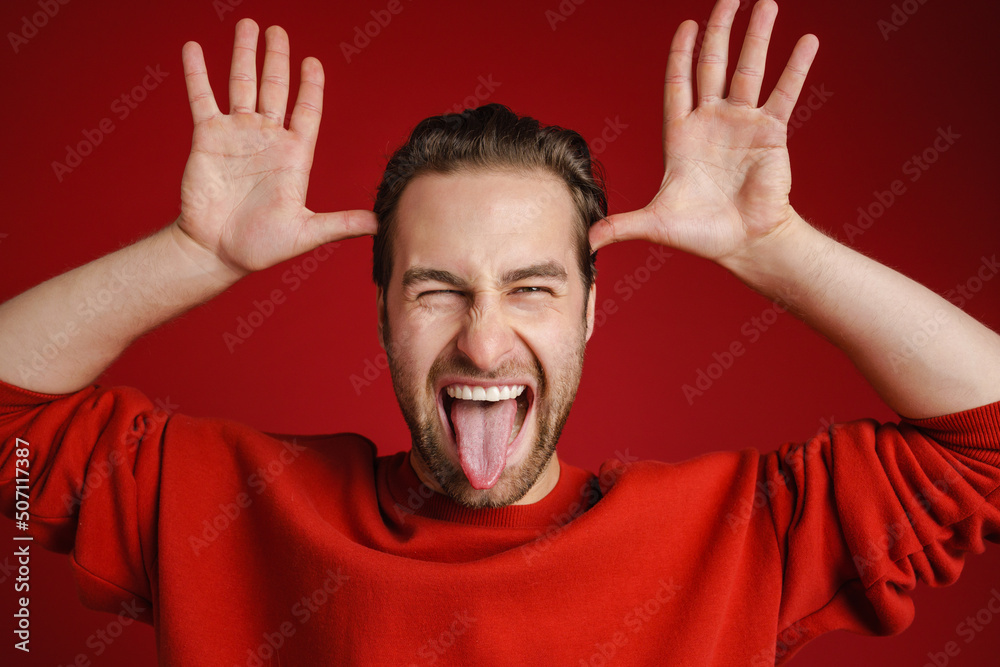 Young bristle man wearing sweater gesturing while showing his tongue - obrazy, fototapety, plakaty 