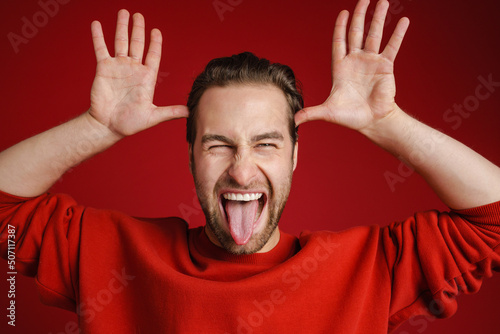 Canvas Print Young bristle man wearing sweater gesturing while showing his tongue