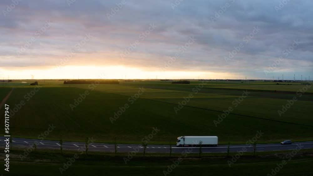 Logistics and transportation of Container. Semi trucks driving on a highway into the sunset. Cargo truck with cargo trailer driving on a highway. White Truck delivers goods. Aerial. Drone. Logistics and transportation of Container. Semi trucks driving on a highway into the sunset. Cargo truck with cargo trailer driving on a highway. White Truck delivers goods. Aerial. Drone.