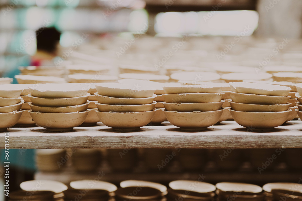 Many small round plates made of ceramic clay. Ceramic cup in rack prepare for cleans with sandpaper before applying the pattern on the clay product. handicraft and small business concept.