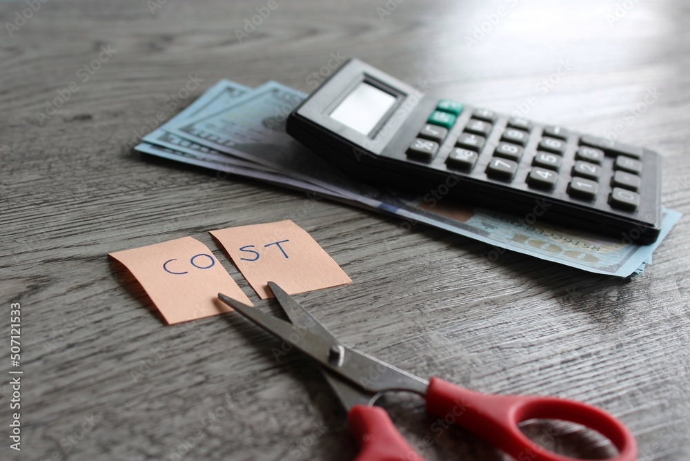 Scissor, calculator, money and note with text COST. Financial, cost cutting, reduce expenses concept Scissor, calculator, money and note with text COST. Financial, cost cutting, reduce expenses concept