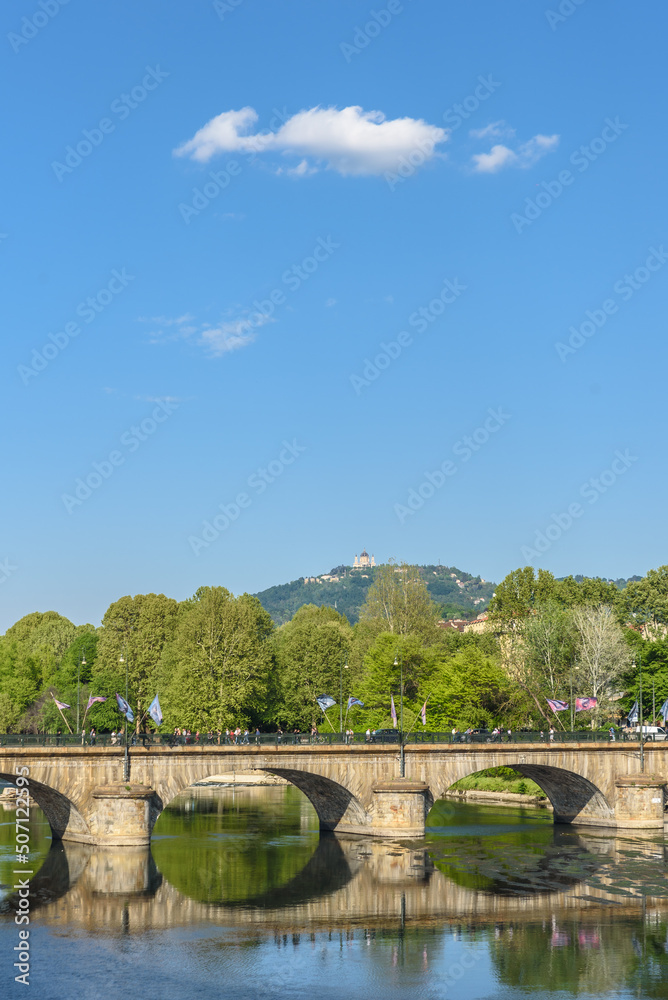 View of the Po river and the Vittorio Emanuele I bridge. In the distance is to see the hill with the Basilica of Superga. Vertical image. Turin, Italy. May 1, 2022.